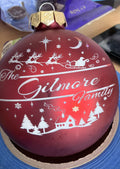 Red glass bauble engraved with The Gilmore Family, reindeer and a snowy village