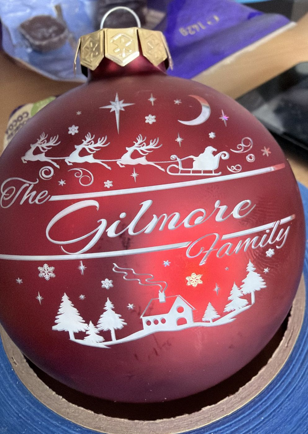 Red glass bauble engraved with The Gilmore Family, reindeer and a snowy village